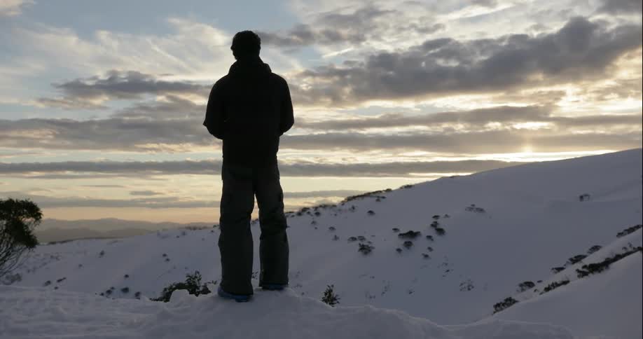 Man stands on a snowy mountain watching the sunset