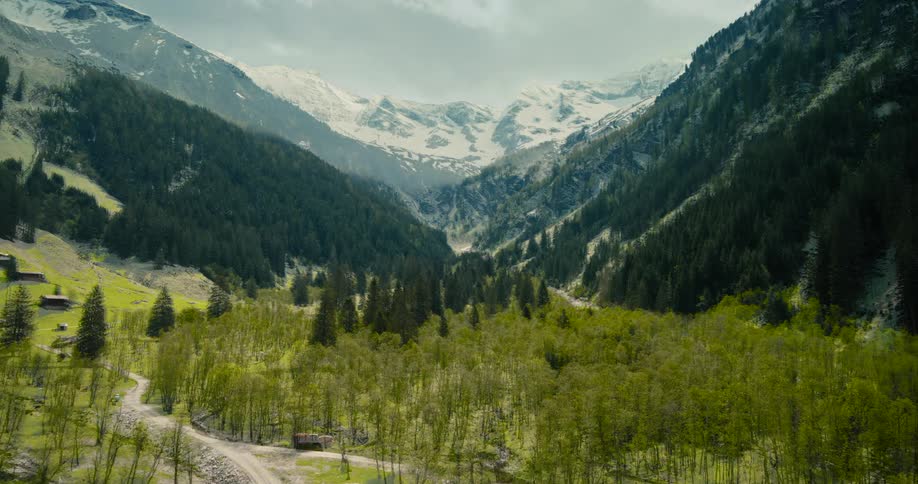 Roads and houses in the snow covered forested mountain valley as snow melts and leaves appear on trees