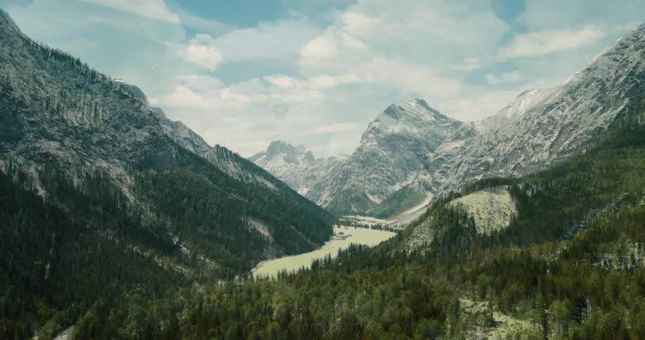 Aerial view of a lush mountain valley surrounded by tall rugged peaks under bright sky