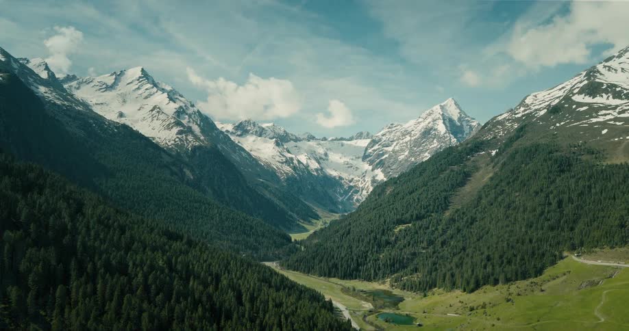 Aerial view of snow covered forested mountains with a road and a stream running through the valley with snow melting and trees on the mountains turning green
