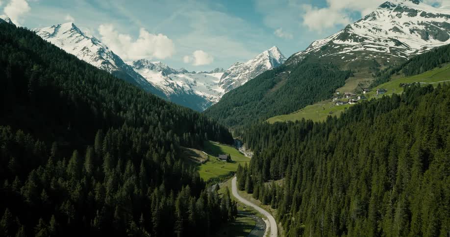 Aerial view of snow covered forested mountains with a road and a stream running through the valley with snow melting and the mountains turning green