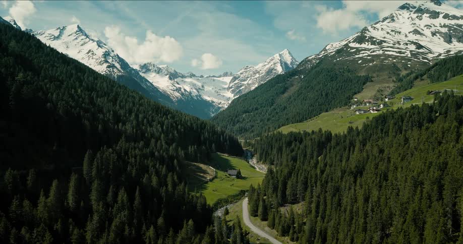 An aerial shot of a deep mountain valley shows the landscape rapidly changing from a snowcovered winter scene with white trees to a lush green summer scene revealing a winding road and a small river between the slopes