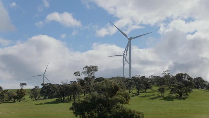 Wind turbines turn behind the trees on the hills
