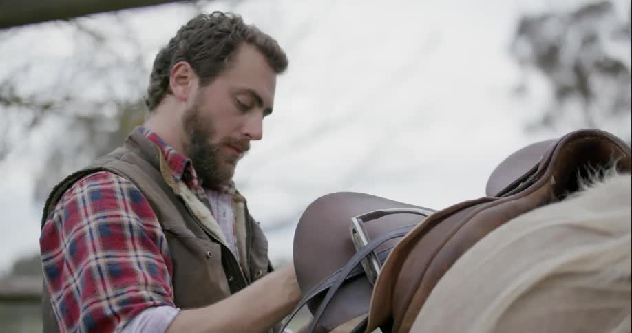 A man attaches a saddle to a horse
