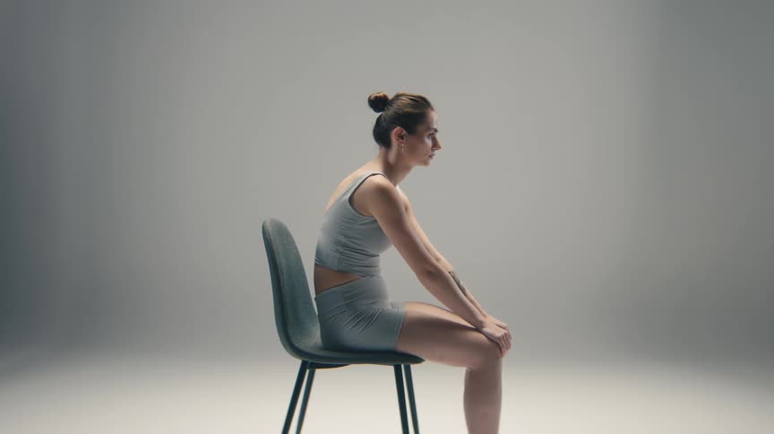 A young woman in athletic wear sits with slumped posture on a chair in a studio