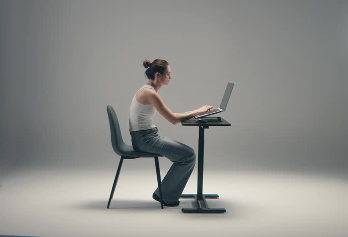 Woman seated in profile typing on a laptop on an adjustable desk