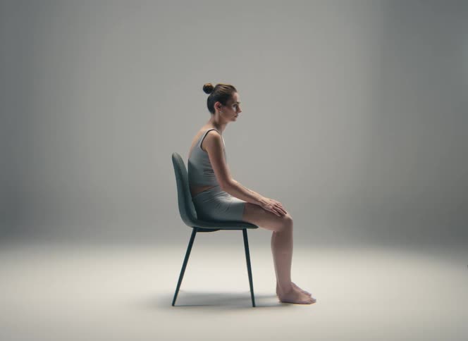 Woman sits in a chair in a gray leotard with her hands on her knees