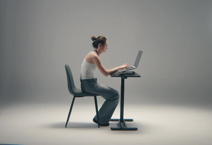 Woman sitting in a chair at a small table typing on a laptop computer
