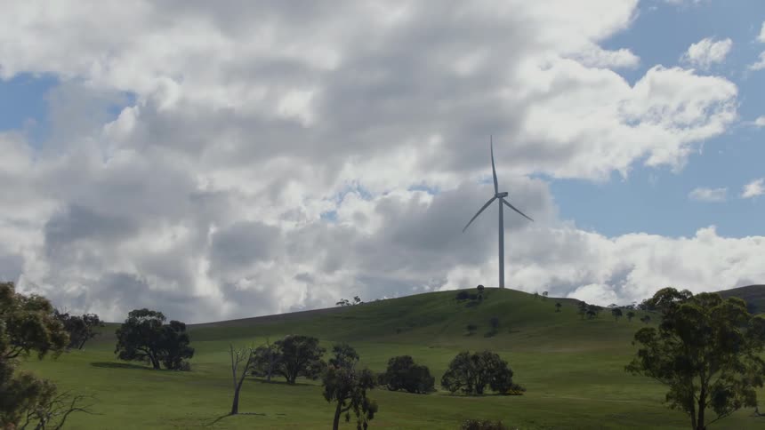 A wind turbine rotates on top of a grassy hill