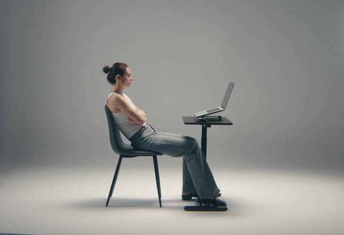 Woman sitting in a chair with her arms folded as she looks at the laptop computer on the table