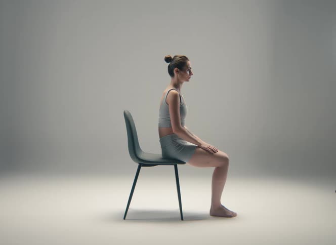 Woman sits upright on a chair in the studio with a plain gray background