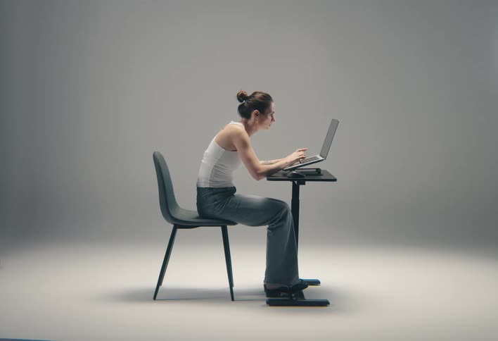 Woman typing on a laptop on an adjustable desk with torso leaning forward