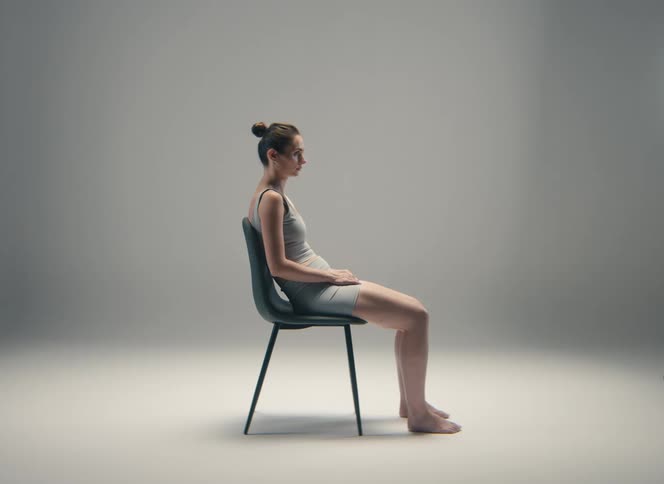 Woman seated in profile on a chair with legs extended forward