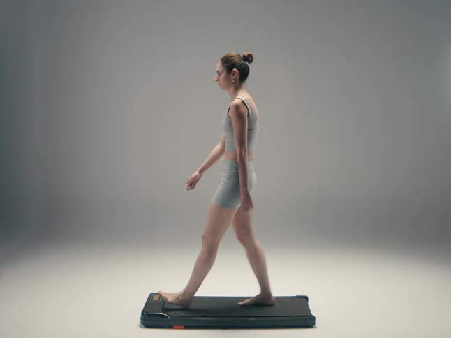 Woman wearing workout clothes walks on a treadmill in a nearly empty room