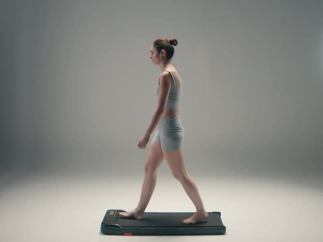 A young woman walks on a treadmill indoors dressed in active pants for her workout
