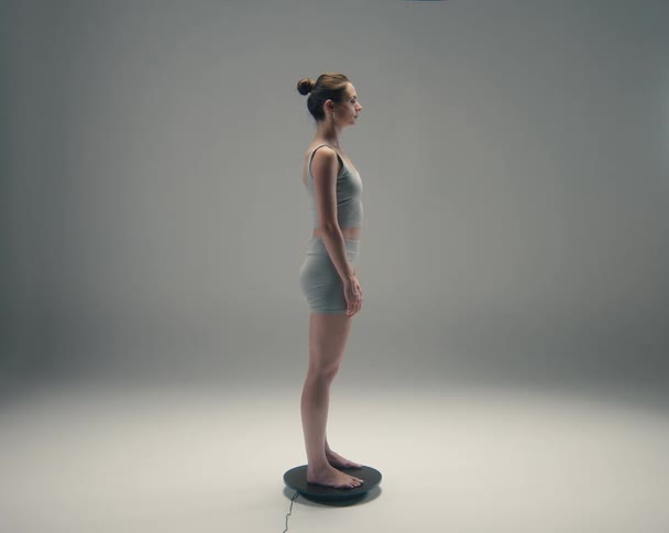 A female is standing on a black circle platform that is turning her body in a circle