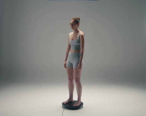 A woman in athletic wear stands on a rotating display platform in a well lit studio