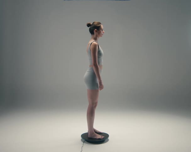 Woman stands motionless on a small rotating platform while wearing a gray outfit