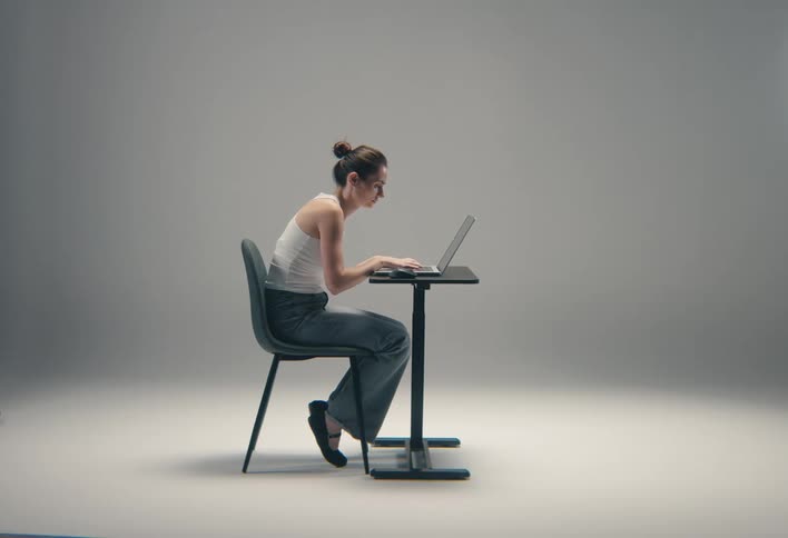 Woman sitting in a chair at a small table typing on a laptop computer
