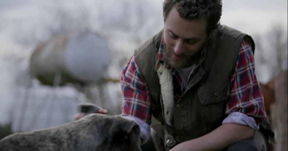 A man pets a dog in a rural area