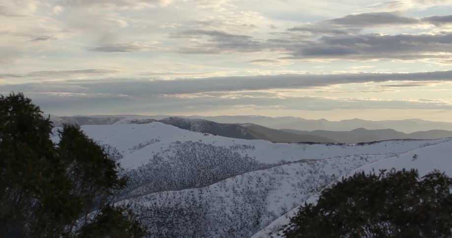 Birds fly over snowy hills on a windy day