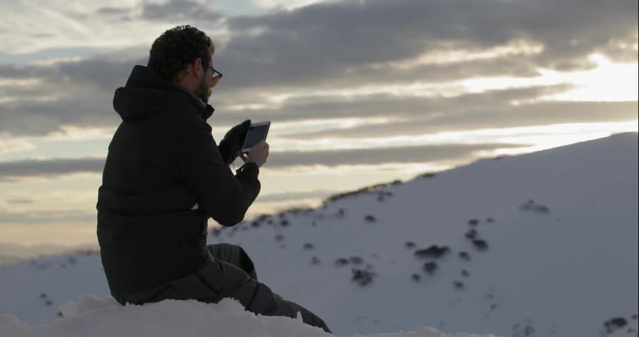 Man sitting in snow taking picture of snow covered surroundings