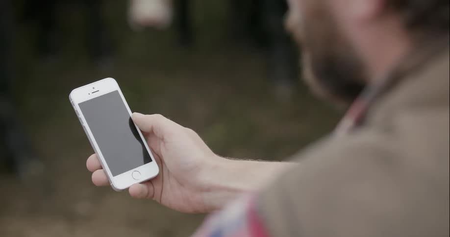 A man is holding a cell phone pressing the screen