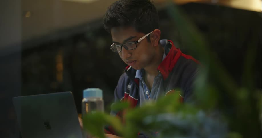 A man is sitting down using a laptop and writing things down