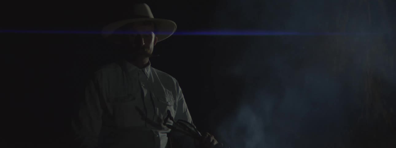 Man stands next to a smoking fire while outdoors at night