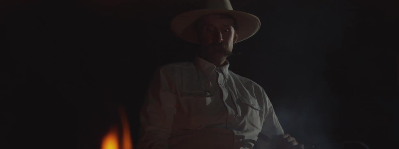 Man wearing a widebrimmed hat seated in a dark setting
