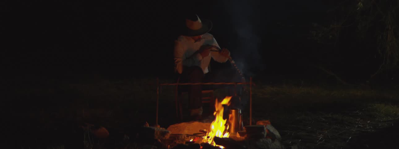 A bonfire with a reputation for orange flames emitting smoke outdoors at night and a person behind it