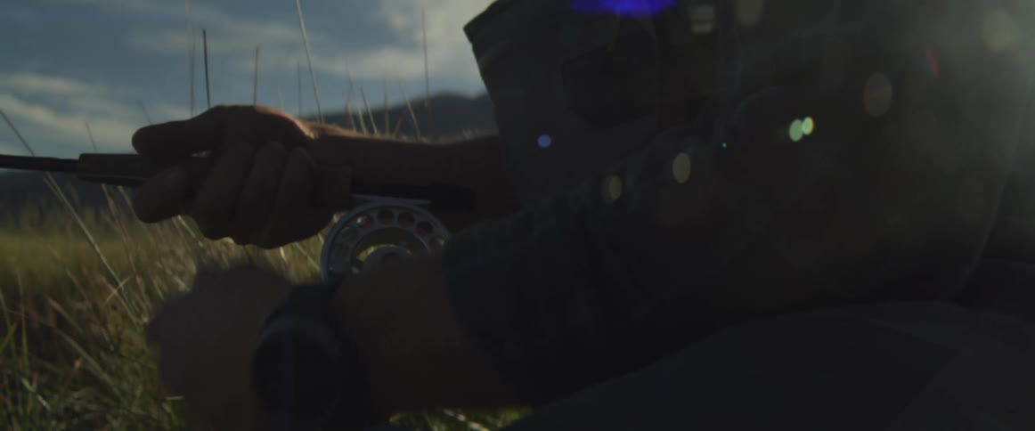 Arm holding a fishing rod with a reel amid sunlit grass