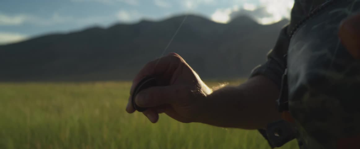 Hand holding a thin line beside a camouflaged bag in an open area