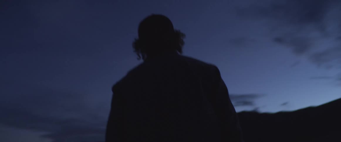 Silhouette of a person wearing a cap appears in front of mountains at dusk