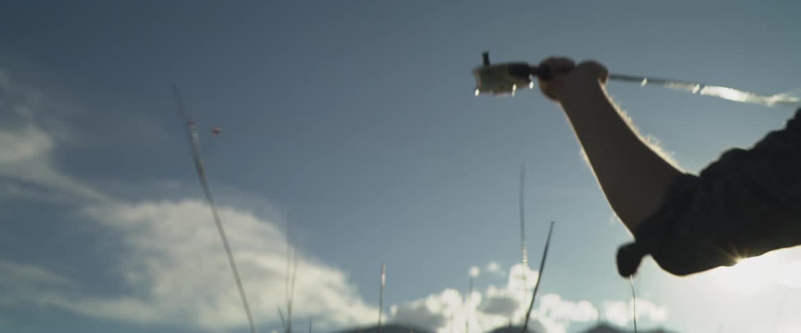 Arm holding a fishing rod with a reel under a bright sky