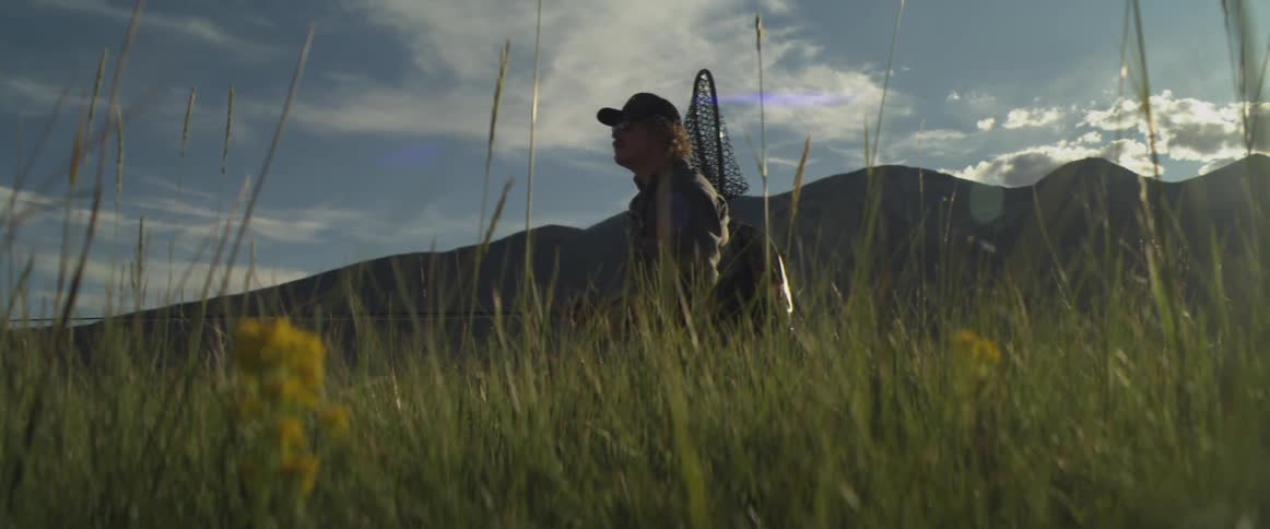 A man is standing in a field with tall green grass looking to his left