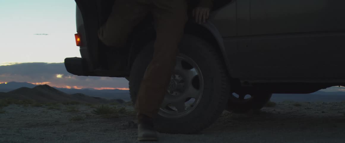 A person walks past the tire of a parked van at dusk