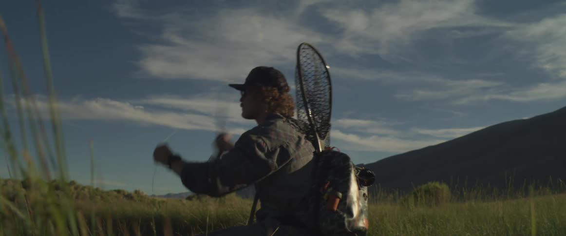 Man fishing swings his fishing pole with a fishing net on his back