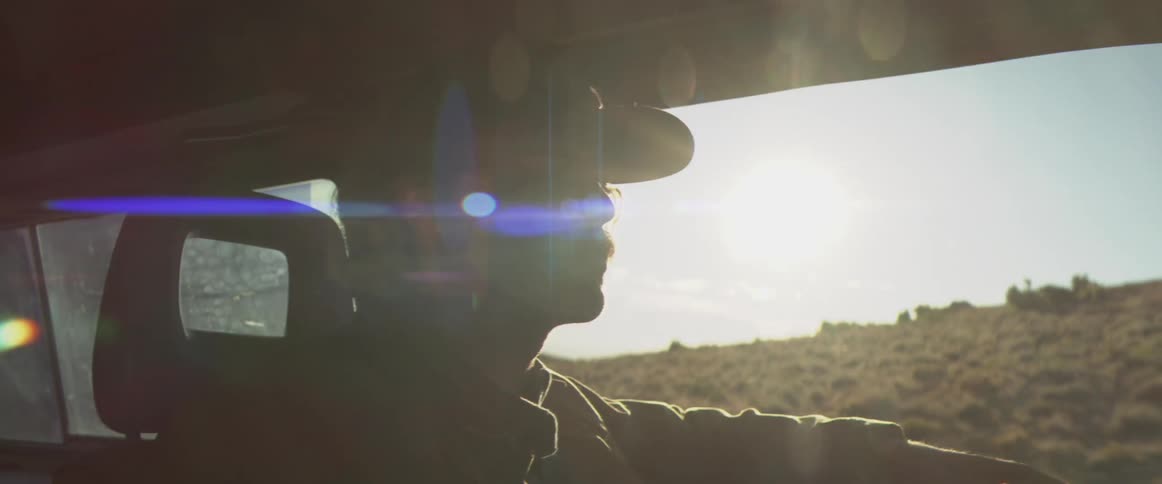 Man wearing a cap driving a vehicle in an arid area under strong light