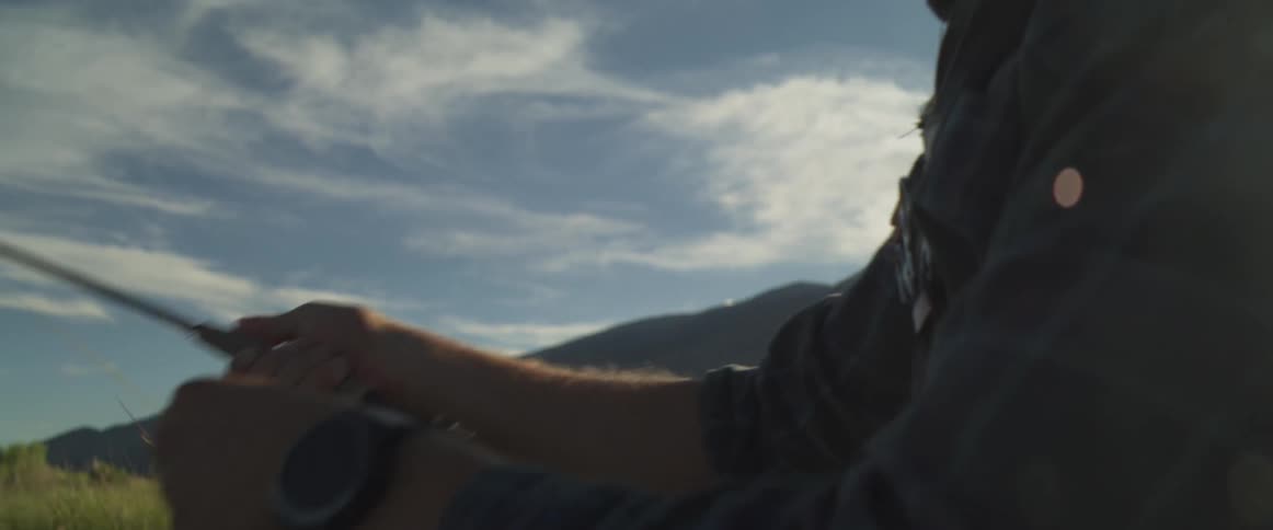 Man casts his fishing line while in a field located near a mountain
