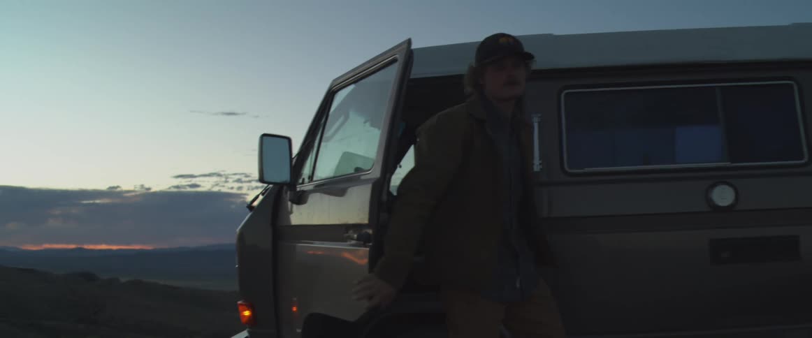 A man exits the drivers seat of a van and walks away at dusk