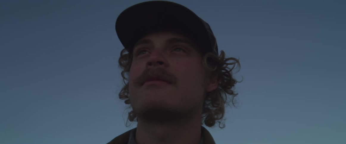 The man is standing by a green hill at sunrise
