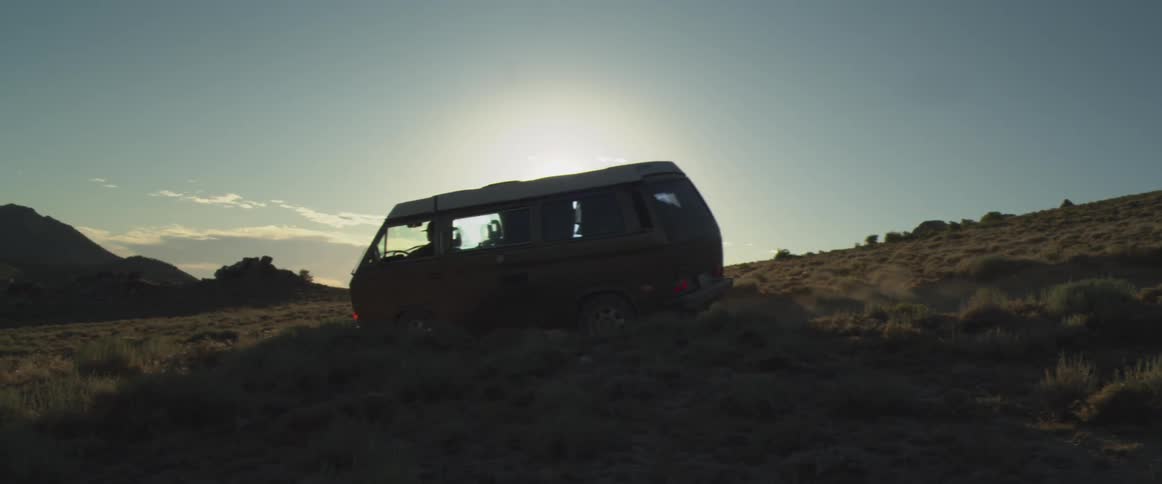 Dark van driving over uneven terrain at sunset