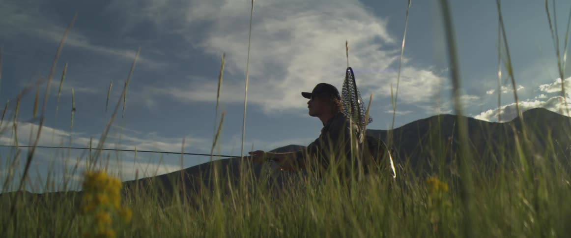 The man is casting his fishing line from the tall grass