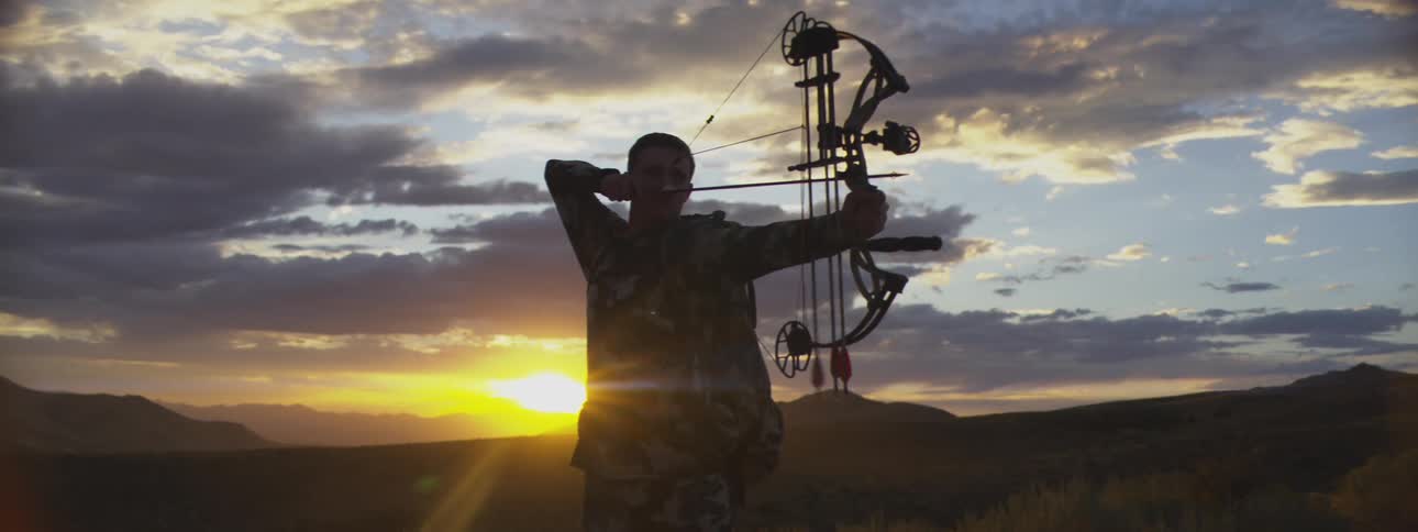 The silhouette of a person in the dark morning pointing an bow forward