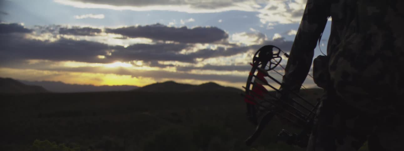 Man stands outside holding his archery equipment as he looks at the mountains