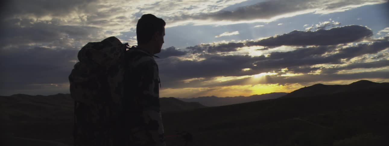 Man in camouflage gear observing the sunset over hills