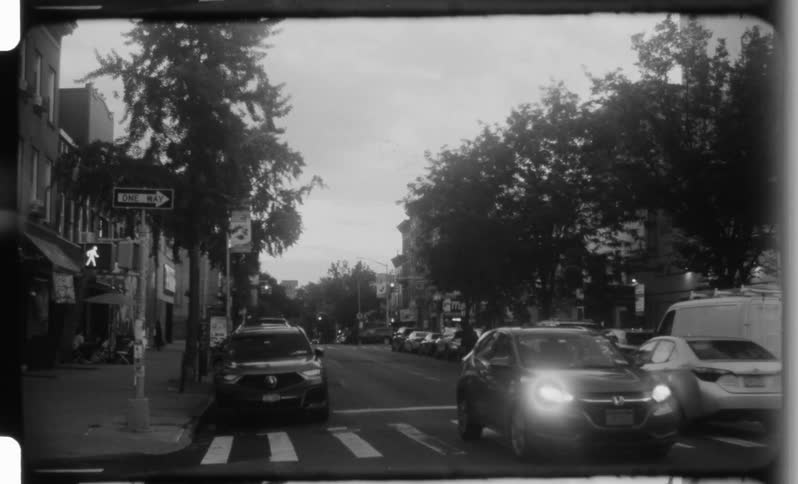 Blackandwhite urban scene with cars crossing an intersection lined with trees and storefronts
