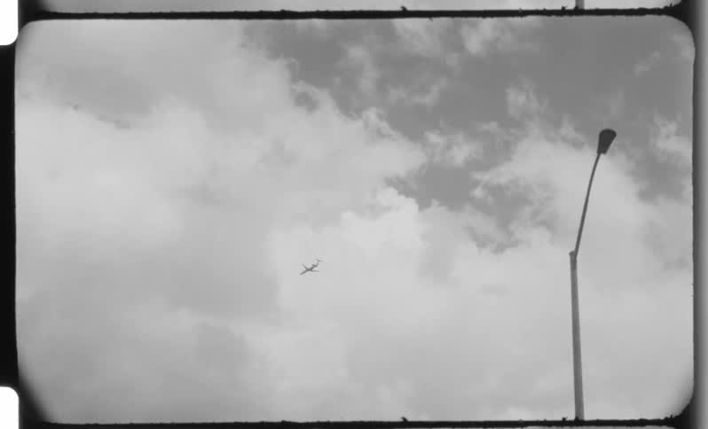 Airplane crosses the cloudy sky beside a light pole