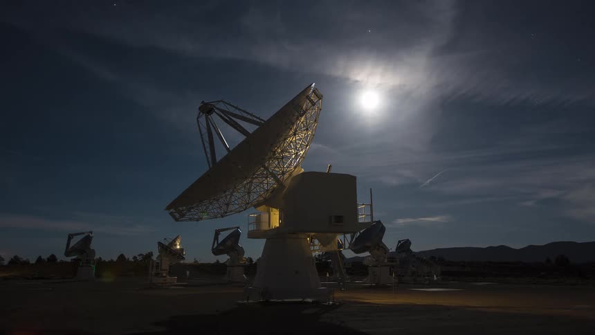 Satellite dish illuminated at night with other antennas visible in the distance